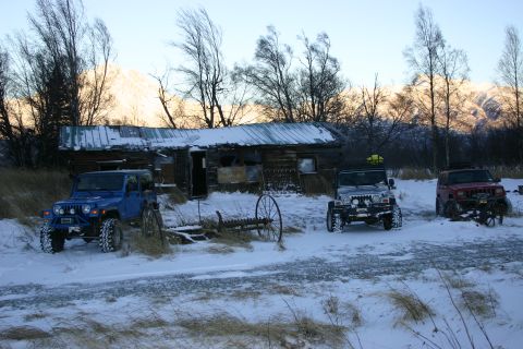 2003 Jeep TJ - Three Jeep Wranglers are parked in the snow outside a weathered cabin, with mountains in the background.