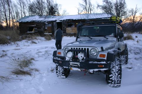 2003 Jeep TJ - A silver 2003 Jeep TJ Rubicon is parked in the snow outside a dilapidated wooden cabin.