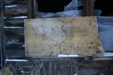 2003 Jeep TJ - A weathered wooden board with graffiti is nailed over a broken window of a rustic building, with snow on the ground.