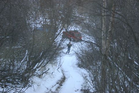 2003 Jeep TJ - A red SUV is stuck in the snow and trees, with a person standing on the path nearby.