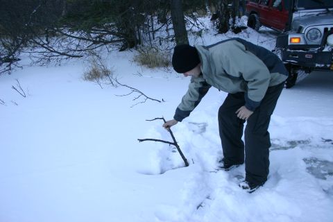 2003 Jeep TJ - A man interacts with a stick in the snow near a silver Jeep Wrangler and a red Jeep Cherokee.