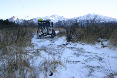 2003 Jeep TJ - A Jeep TJ navigates a snow-covered path towards , snow-capped mountains under a clear sky.