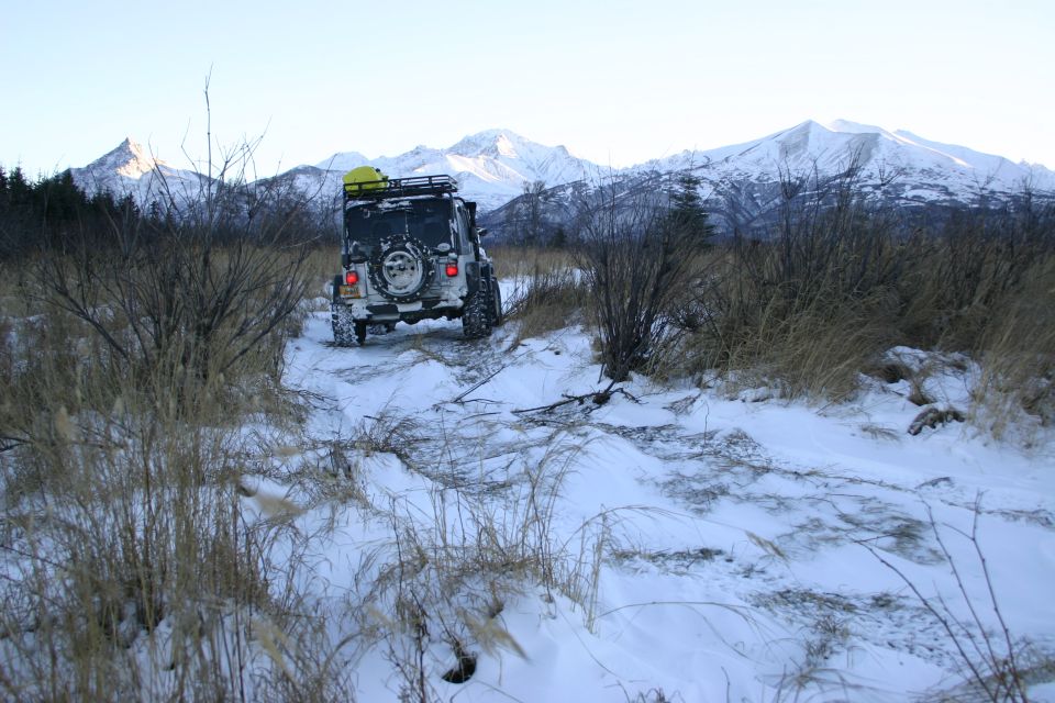Jeep TJ driving on a snowy trail with mountains in the background