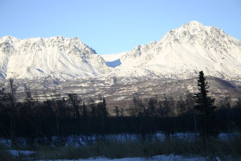 2003 Jeep TJ - A vast winter landscape features snow-capped mountains and a dense forest in the foreground, under a bright blue sky.