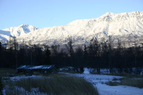 2003 Jeep TJ - A winter scene with snow-covered mountains in the background and two old cabins in the foreground, set against a backdrop of dark trees.