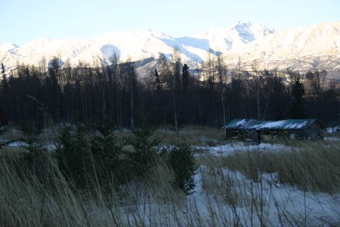 2003 Jeep TJ - An old cabin rests in a winter landscape, with snow-covered mountains looming behind.