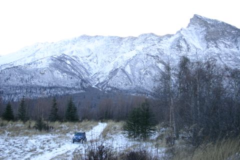 2003 Jeep TJ - A Jeep Wrangler drives on a snowy trail with a large, snow-covered mountain range in the background.