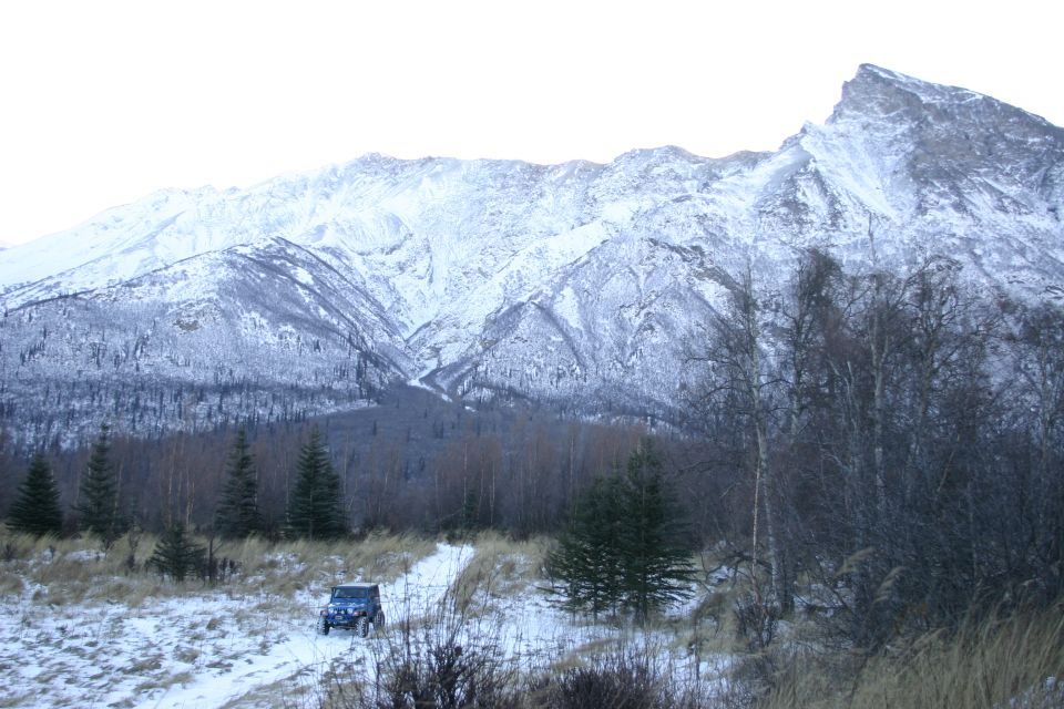 Jeep Wrangler on snowy path with snow-covered mountains behind