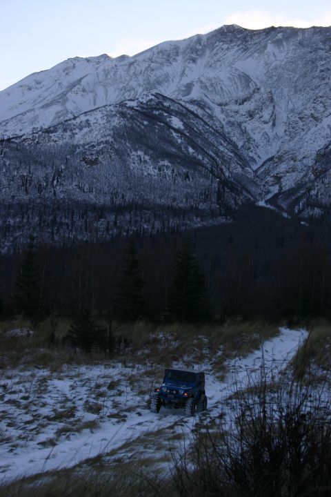 2003 Jeep TJ - A blue Jeep Wrangler navigates a snowy path with a , snow-capped mountain range looming behind it.
