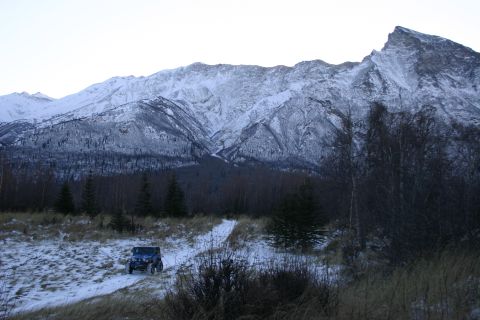 2003 Jeep TJ - A blue 2003 Jeep TJ navigates a snowy path with a backdrop of , snow-capped mountains.