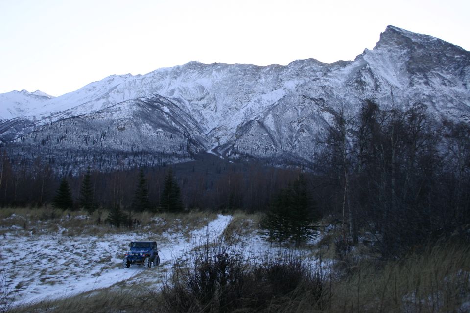 Blue 2003 Jeep TJ on a snowy trail with snow-covered mountains behind