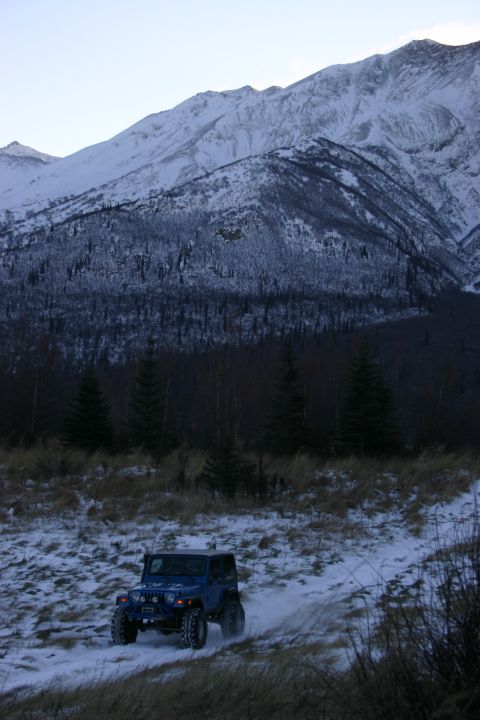 2003 Jeep TJ - Blue 2003 Jeep TJ navigates a snow-covered trail in a mountainous landscape.