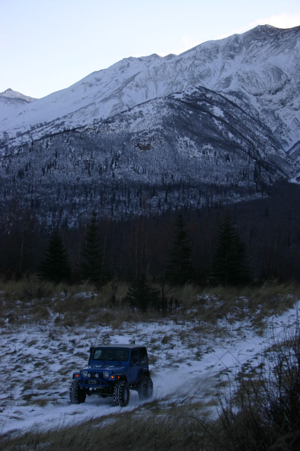 Blue 2003 Jeep TJ driving on a snowy trail with mountains in the background