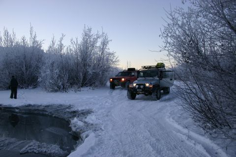 2003 Jeep TJ - Two Jeeps navigate a snow-covered path with frosted trees and a partially frozen body of water.