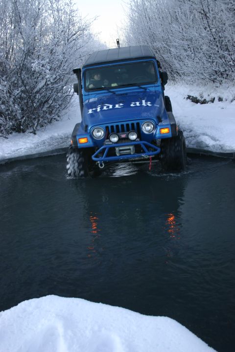 2003 Jeep TJ - A blue Jeep Wrangler navigates through a water crossing in a snowy, wooded area.