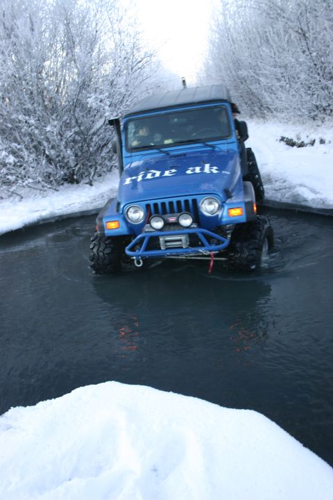 2003 Jeep TJ - A blue 2003 Jeep TJ navigates through a water crossing in a snowy environment.