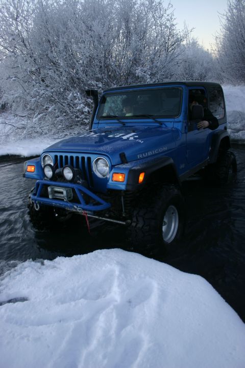 2003 Jeep TJ - A blue 2003 Jeep TJ Rubicon navigates a snowy, watery terrain, its off-road capabilities.
