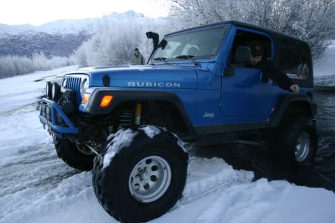 2003 Jeep TJ - A blue Jeep Wrangler navigates a snowy, icy terrain with a snorkel and off-road tires.