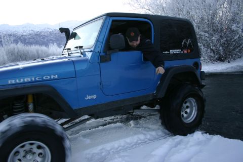 2003 Jeep TJ - A blue 2003 Jeep TJ Rubicon navigates a snowy terrain with a driver visible.