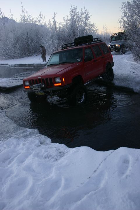 2003 Jeep TJ - Two Jeep Cherokee XJs navigate an icy stream in a snowy landscape.