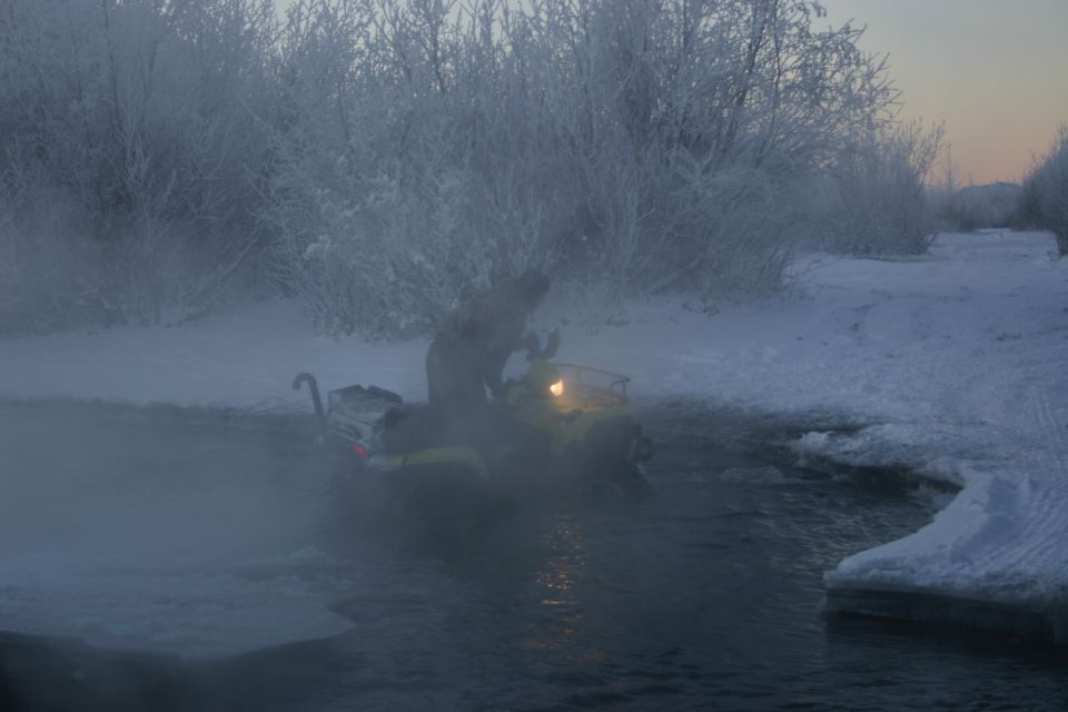 Snowmobile crossing a partially frozen body of water with steam rising