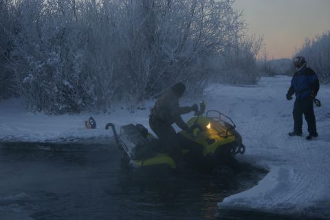 2003 Jeep TJ - A snowmobile enters the water near a snowy bank with trees in the background.