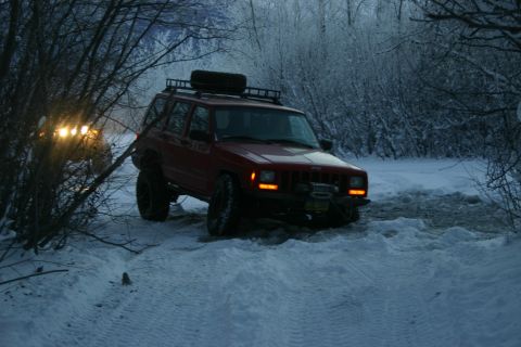 2003 Jeep TJ - A red Jeep Cherokee XJ navigates a snowy trail with another vehicle visible behind it.