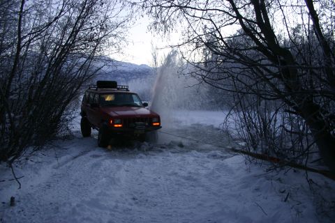 2003 Jeep TJ - A red Jeep Cherokee XJ navigates through a snowy landscape, kicking up water.