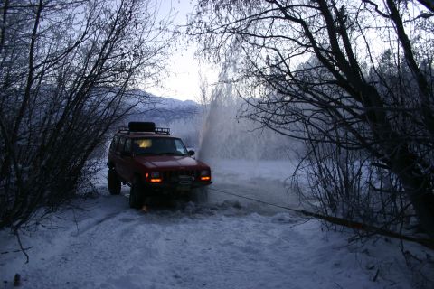 2003 Jeep TJ - Red Jeep Cherokee XJ being pulled from a snowy area with water spray in the background.