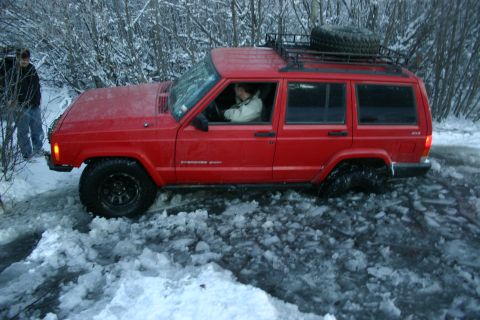 2003 Jeep TJ - A red Jeep Cherokee XJ is stuck in a snowy and icy area, with a person driving and another person observing.