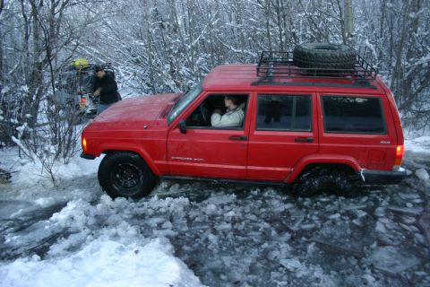 2003 Jeep TJ - A red Jeep Cherokee XJ navigates through a snowy and icy landscape, with another vehicle visible in the background.
