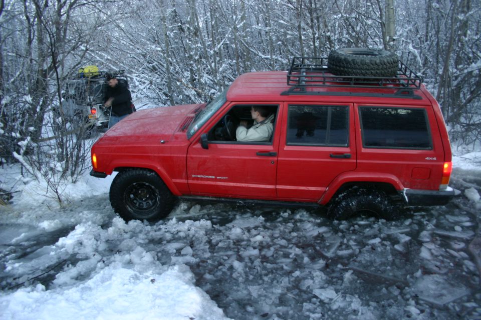 Red Jeep Cherokee XJ with a roof rack and spare tire stuck in icy terrain