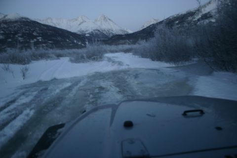 2003 Jeep TJ - A 2003 Jeep TJ navigates a partially frozen stream amidst a snow-covered mountain scene.