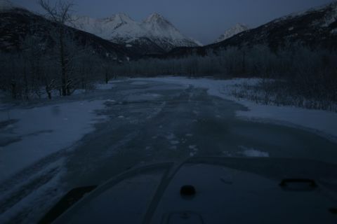 2003 Jeep TJ - The vehicle is driving on a partially frozen road with snow-covered trees and mountains in the distance.