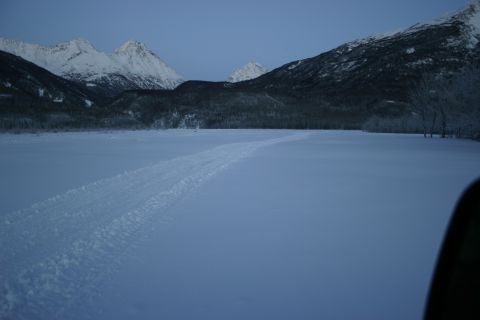 2003 Jeep TJ - Tire tracks mark a path across a snow-covered landscape with mountains in the background.