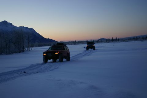 2003 Jeep TJ - Two SUVs traverse a snow-covered field under a twilight sky, with mountains in the distance.