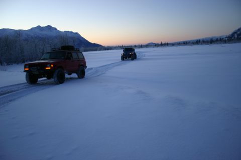 2003 Jeep TJ - Two SUVs traverse a snow-covered landscape under a twilight sky, with mountains visible in the distance.