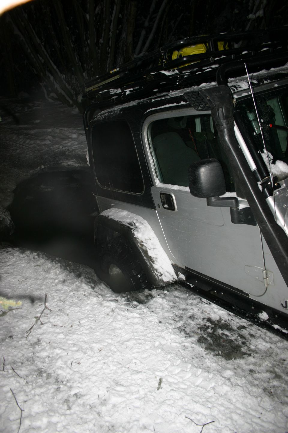 Silver Jeep TJ with snorkel and roof rack stuck in snow