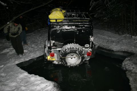 2003 Jeep TJ - A black 2003 Jeep TJ is partially submerged in water during a snowy night.