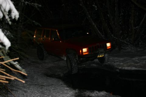 2003 Jeep TJ - A red Jeep Cherokee XJ navigates a snowy trail in the dark.