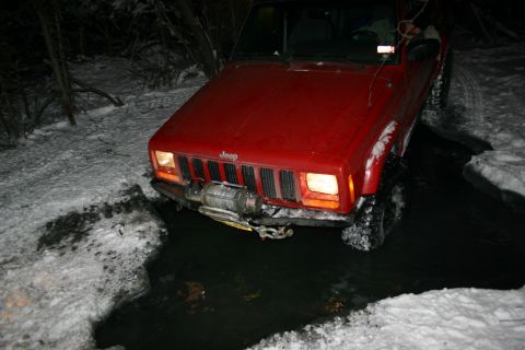 2003 Jeep TJ - A red Jeep Cherokee XJ navigates a snowy and watery path at night.