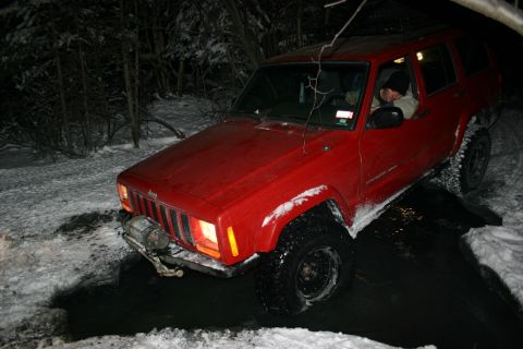 2003 Jeep TJ - A red Jeep Cherokee XJ navigates a snowy and watery path at night.