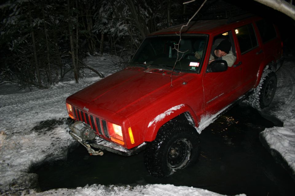 Red Jeep Cherokee XJ driving through snow and water