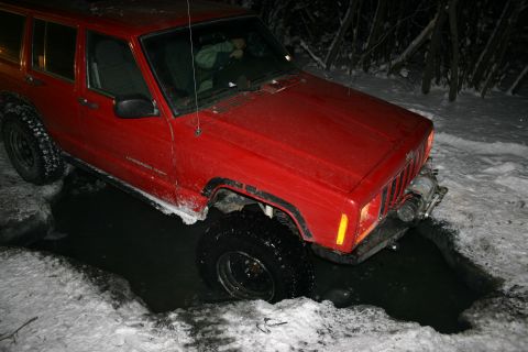 2003 Jeep TJ - Red Jeep Cherokee stuck in a snow-covered hole with water.