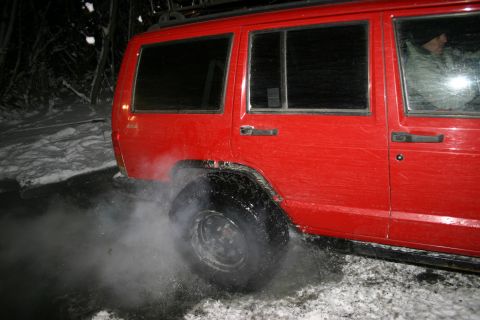 2003 Jeep TJ - A red SUV spins its tires, creating a cloud of smoke and spray in a snowy environment.
