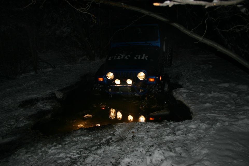 Blue 2003 Jeep TJ with "ride ak" on hood stuck in mud and snow at night