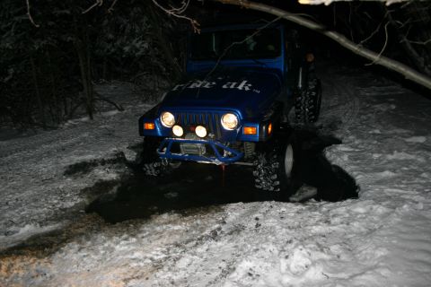 2003 Jeep TJ - A blue Jeep Wrangler navigates a snowy path in the dark, with 'ride ak.' visible on its hood.