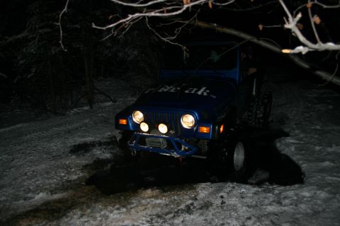 2003 Jeep TJ - A blue Jeep Wrangler with "ride ak" visible on its hood is parked on a snowy trail at night.