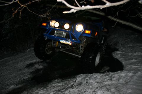 2003 Jeep TJ - A blue 2003 Jeep TJ navigates a snowy trail at night, equipped with a heavy-duty aftermarket bumper and winch.