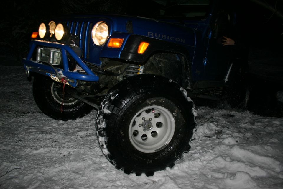 Blue 2003 Jeep TJ Rubicon with aftermarket bumper, winch, and auxiliary lights in snow